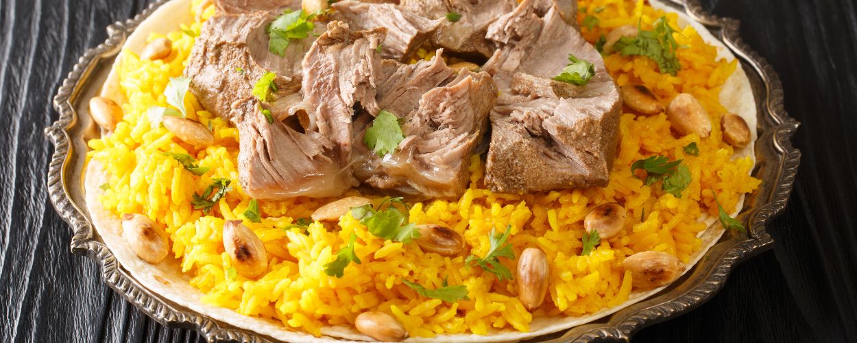 Plate of yellow spiced rice with braised lamb chunks, peanuts, and cilantro on an ornate platter.