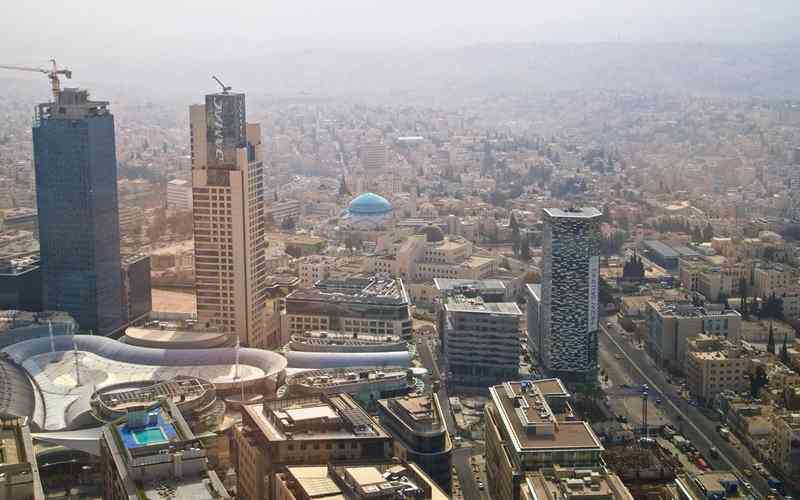 Aerial cityscape with tall skyscrapers, a blue-domed building, and curved white-roofed structures in the foreground.",