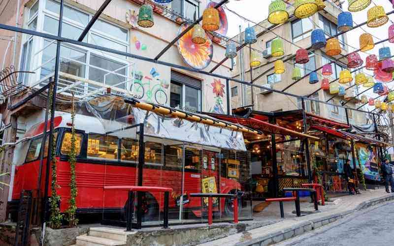 Colorful street cafe built from a red bus with string lights and hanging lanterns overhead.
