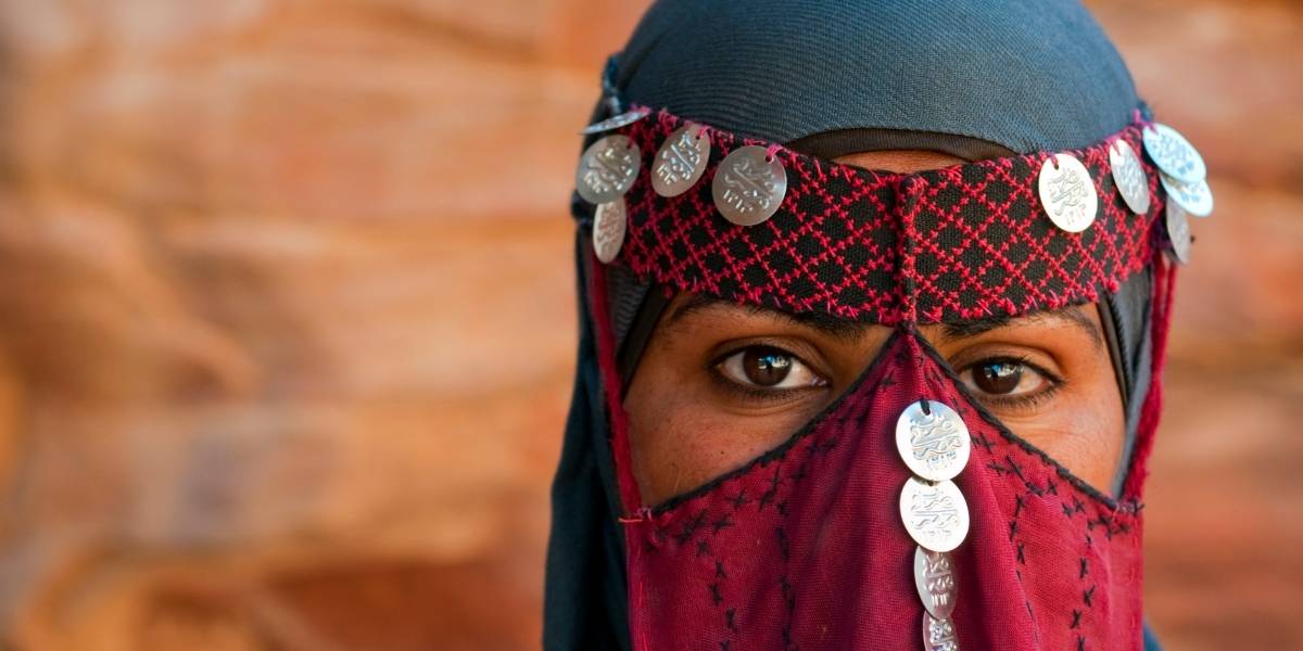Close-up of a person wearing a red patterned headband with hanging silver coins and a matching veil, only the eyes visible.