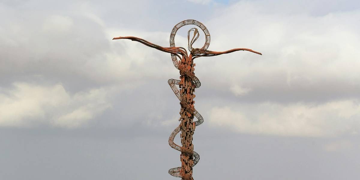 Tall sculpture of a human figure with outstretched arms, built from intertwining wooden and metal rings reaching toward the sky