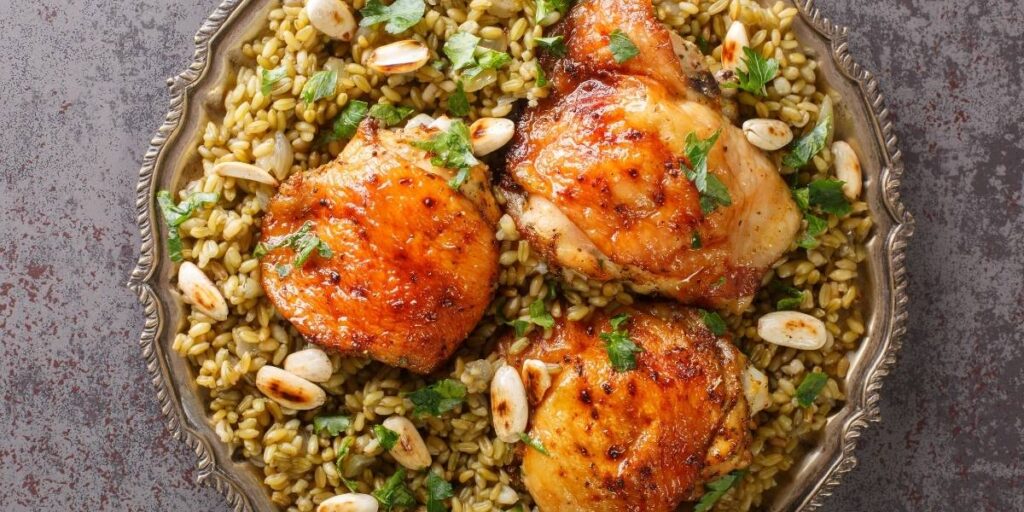 78 | Ordonna Guide Roasted chicken thighs and breasts atop farro with almonds and chopped parsley on a decorative plate.