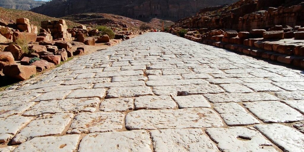 Ancient stone road stretching into a desert canyon, with rocky walls and ruins on both sides.