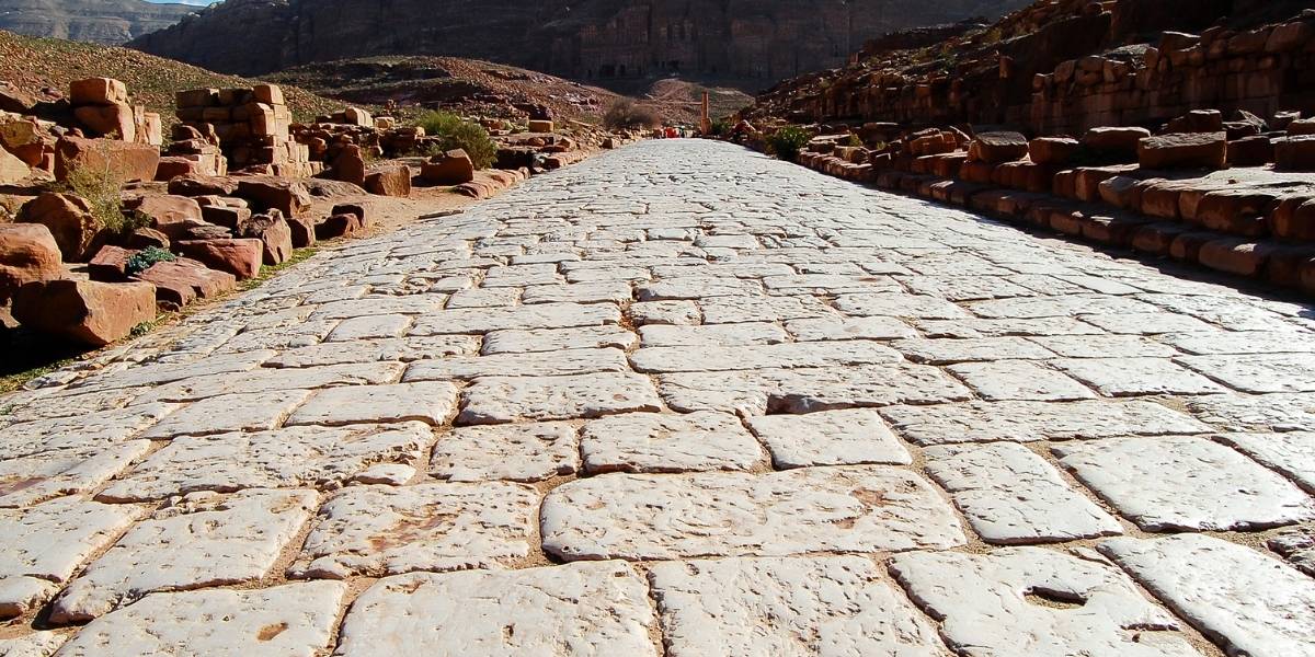 Ancient stone road stretching into a desert canyon, with rocky walls and ruins on both sides.