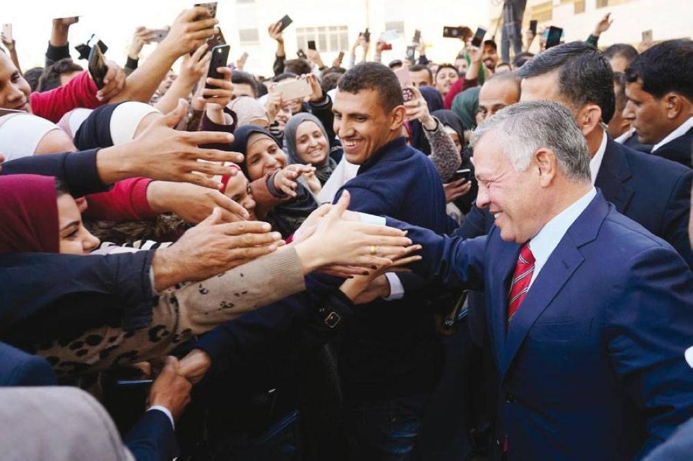 Man in a navy suit greets a crowd, hands reaching out for high-fives and selfies surrounded by cheering supporters with smartphones