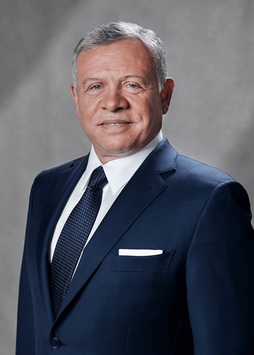 Professional head-and-shoulders portrait of a smiling gray-haired man in a navy suit and tie against a neutral backdrop.