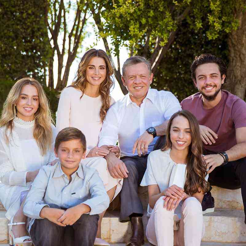 Six-family portrait sitting on steps in a sunny park, smiling together.
