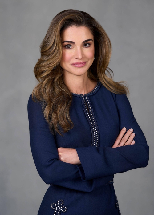 Professional head-and-shoulders portrait of a woman with long wavy hair in a navy dress, arms crossed.