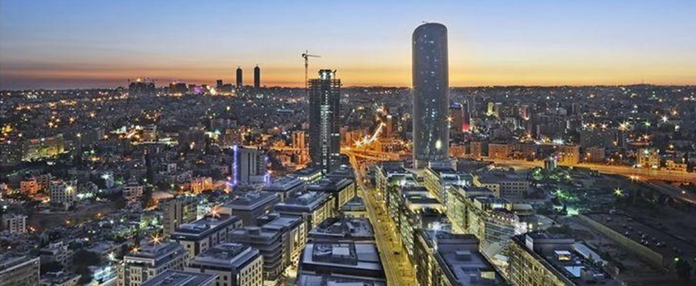 City skyline at dusk with a tall rounded skyscraper under construction and illuminated streets below