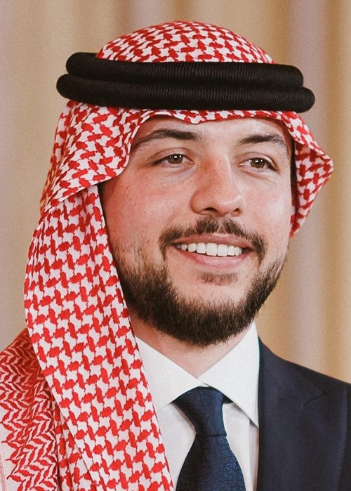 Smiling man wearing a red-and-white checkered keffiyeh and dark suit, white shirt, and blue tie.