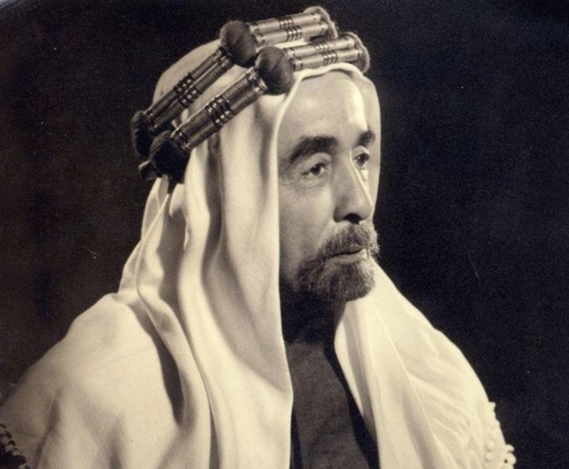 Portrait of a man wearing a white robe and headscarf with hair curlers, looking to the right side of the frame.