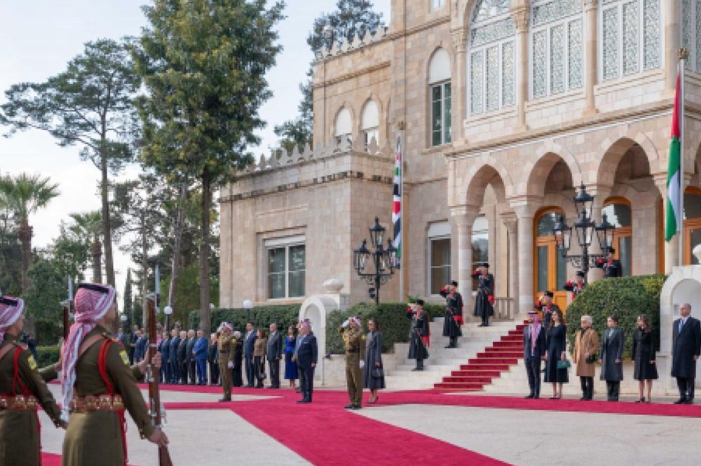 Formal state ceremony on a red carpet outside a stone government building, with officials and guards standing in formation beneath flags.