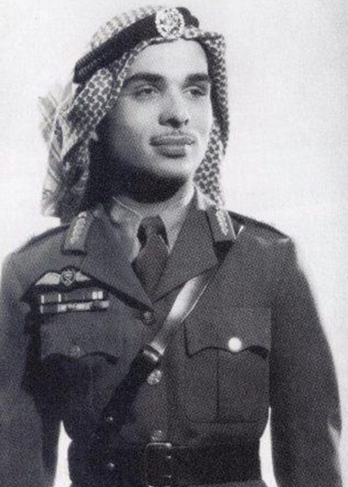 Portrait of a man in a formal military uniform, wearing a ghutra/keffiyeh headscarf and ceremonial sash with medals visible on the chest, looking off to the side.