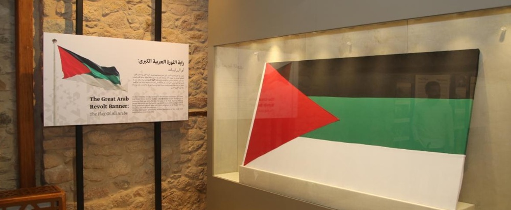 Museum exhibit: large Palestine flag banner in a glass display case with an information placard beside.